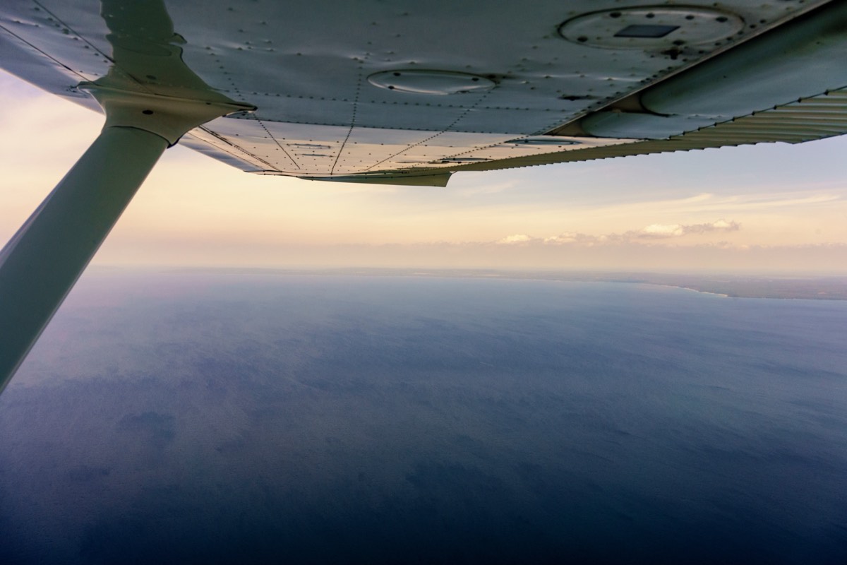 A Navy fighter jet banking over the ocean near an aircraft carrier