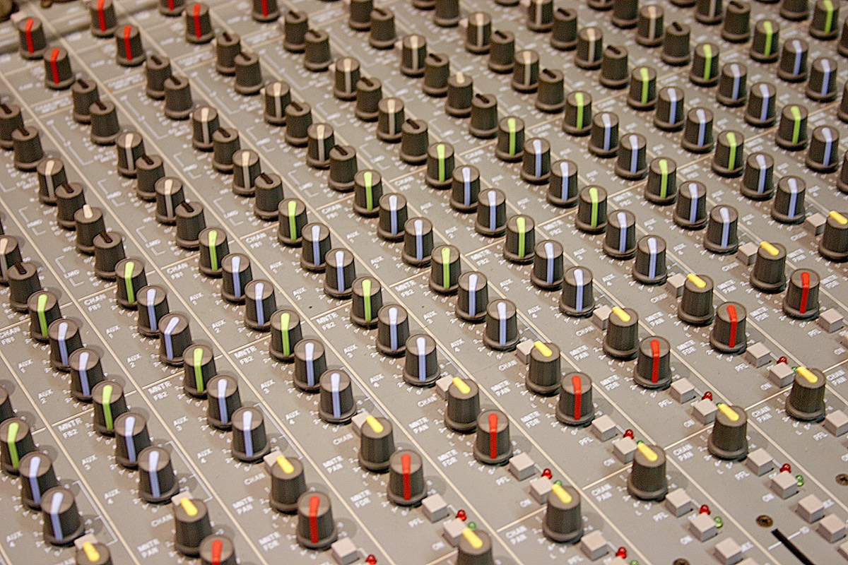 A recording studio mixing console with faders and knobs