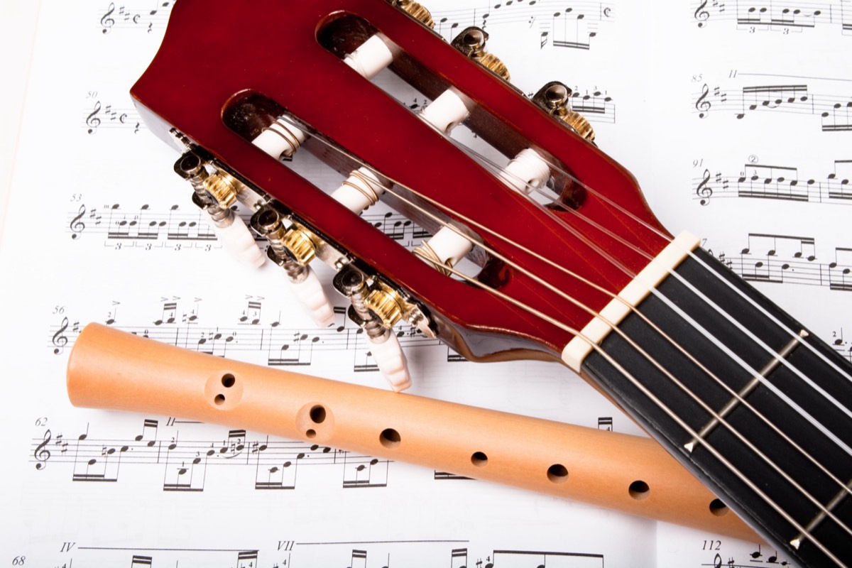An acoustic guitar resting on sheet music in warm light