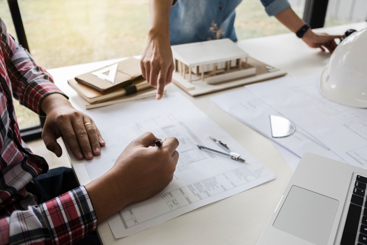 Inventor sketching a product design at a workbench with a prototype and notebook