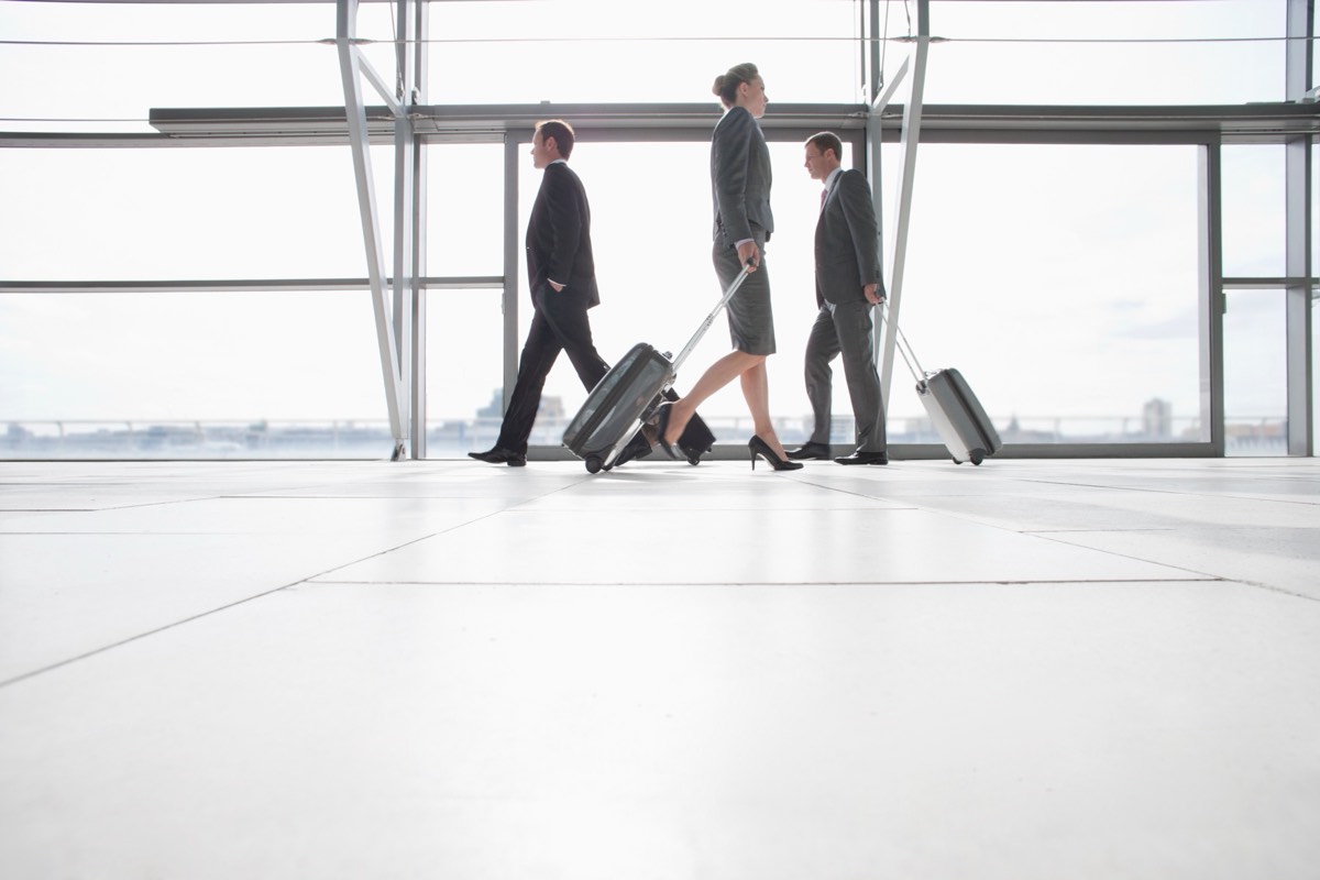 An airport departure terminal with travelers and a rolling suitcase