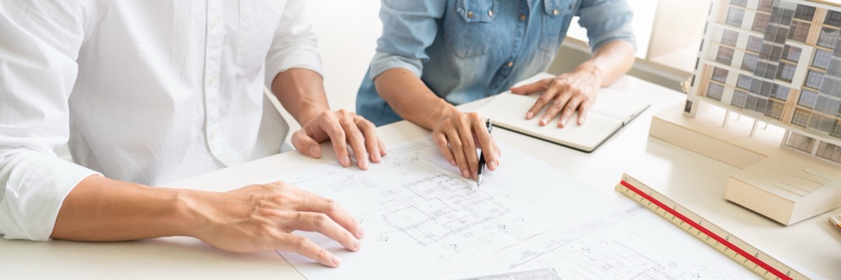 Two business representatives reviewing engineering blueprints across a conference table