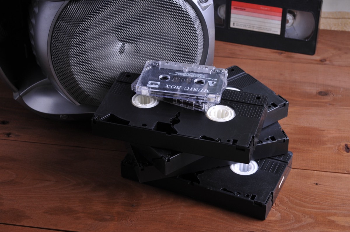 Stacks of unlabeled VHS and video cassette tapes on a shelf